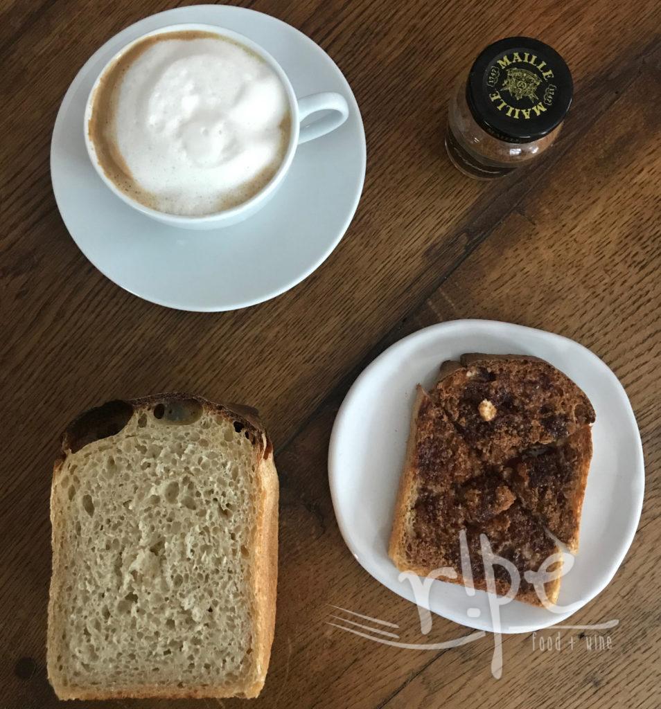 Cinnamon toast on white plate with 3 other items forming a square: sourdough bread slice, coffee with foam, cinnamon sugar in a small Maille jar all on wood grained table