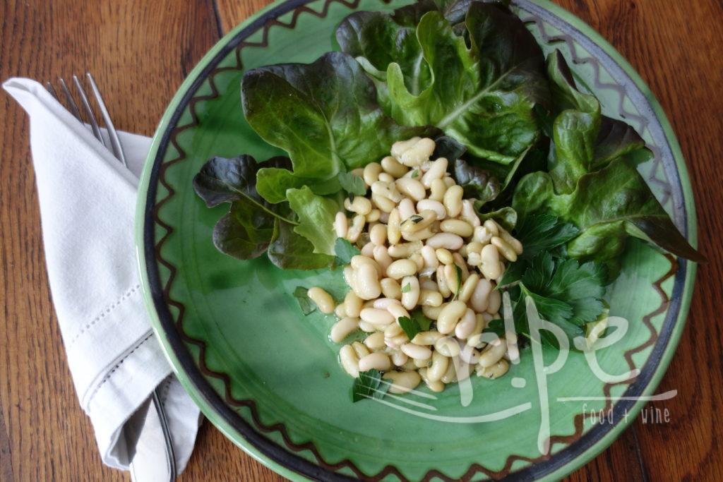 light green beans with leaf lettuce on a green pottery plate on rustic wood table